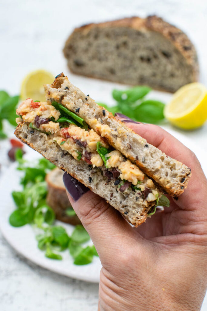 Close-up of a vegan handheld Mediterranean sandwich filled with chickpea spread and salad leaves