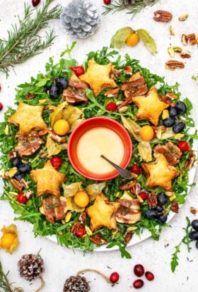 Christmas salad wreath of rocket topped with figs in blankets, goat's cheese pastry stars, physalis, grapes and pecans, with maple lemon dressing in the centre
