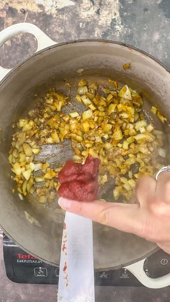 adding tomato pur&eacute;e to onion and spice base