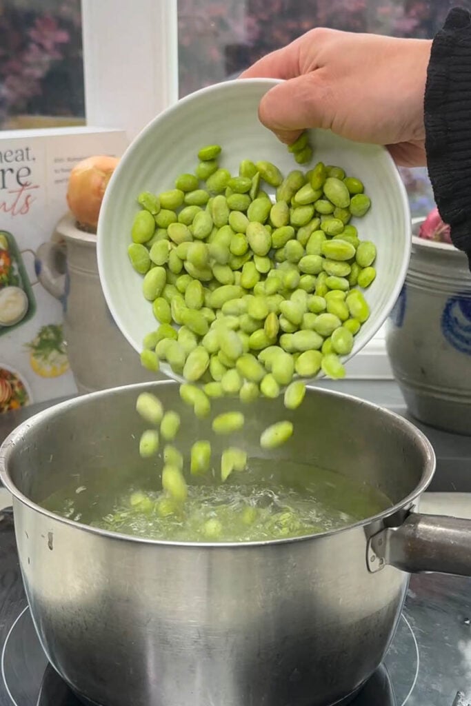 Pouring shelled edamame into a saucepan of boiling water