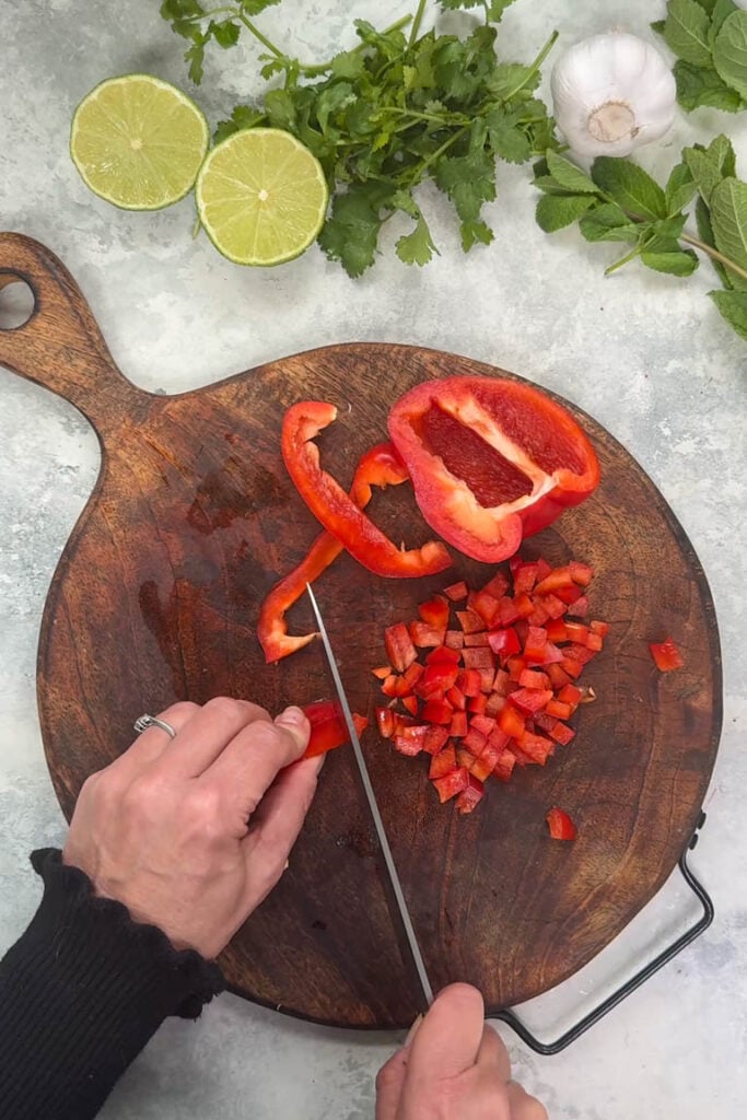 Dicing a red bell pepper into small cubes on a wooden cutting board