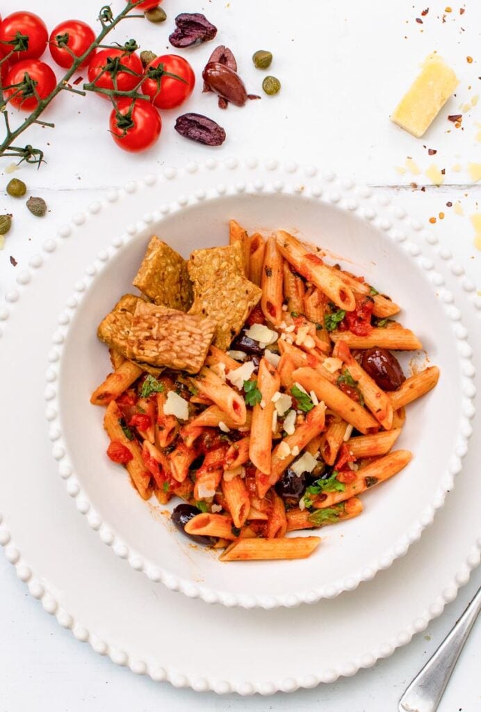 Vegan pasta puttanesca with penne, tempeh, Kalamata olives, capers and fresh basil in a bowl