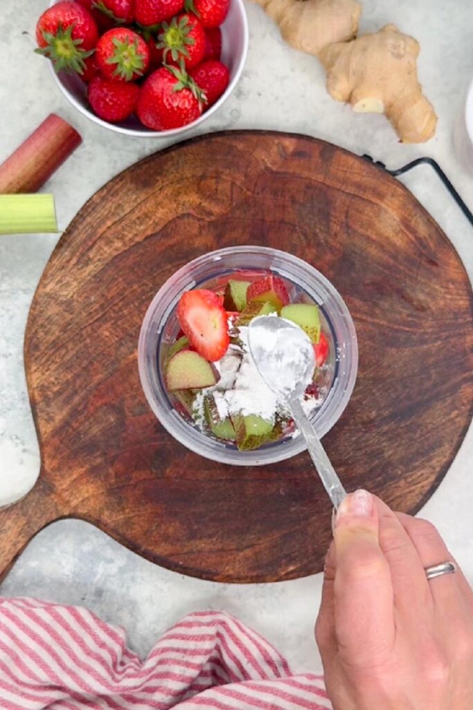 Adding a spoonful of cornflour to chopped strawberries and rhubarb in a blender cup
