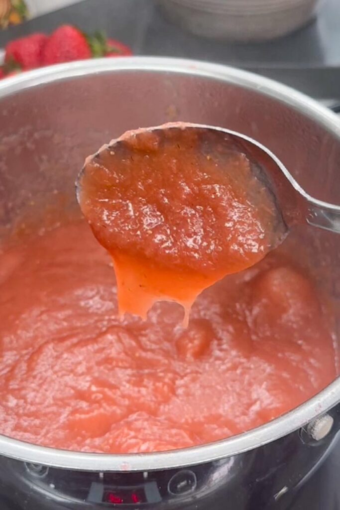 Thick, smooth strawberry and rhubarb filling being lifted by a spoon from a saucepan