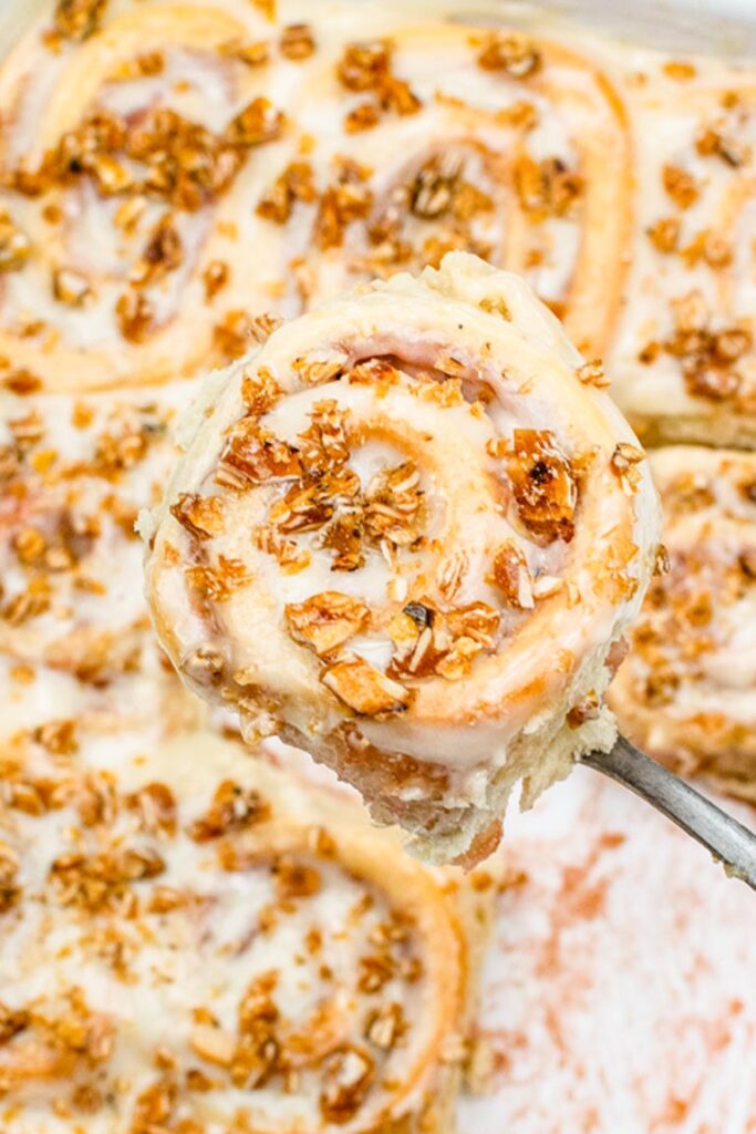 A glazed strawberry rhubarb sweet roll topped with crunchy almond praline being lifted from a baking dish