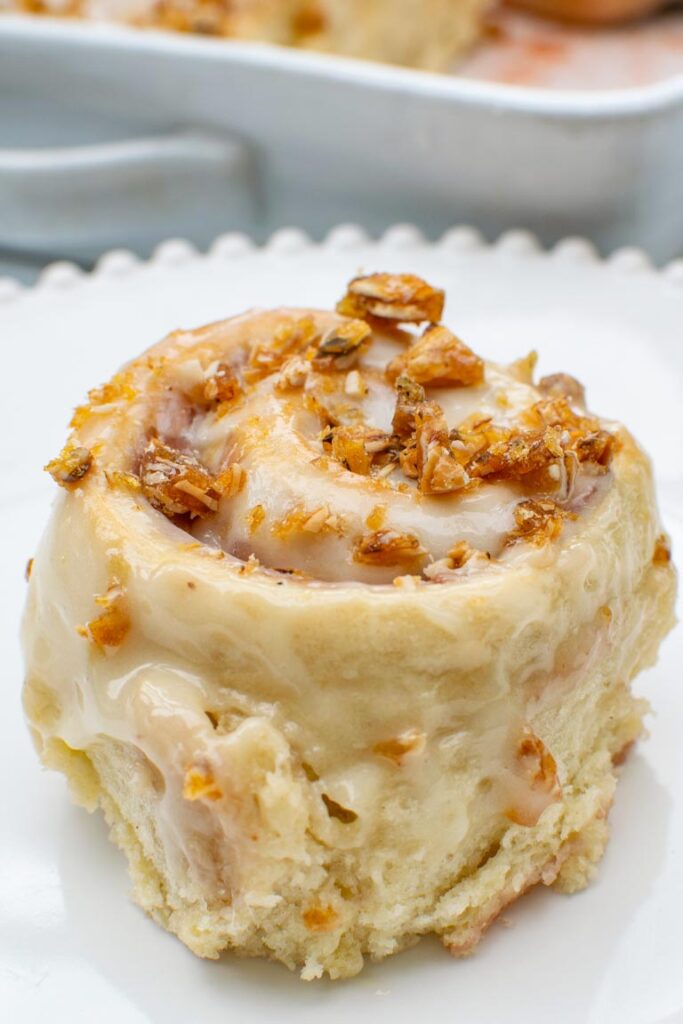 Close up of a strawberry rhubarb sweet roll covered in cream cheese glaze and topped with crunchy almond praline