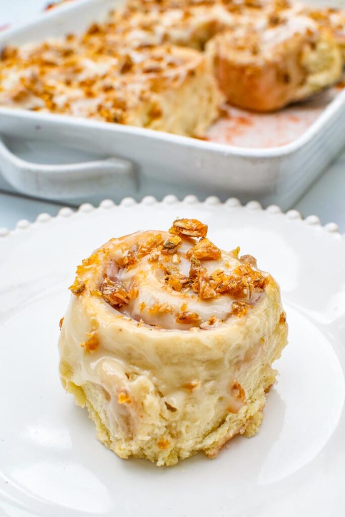 A strawberry rhubarb sweet roll topped with cream cheese glaze and crunchy almond praline
