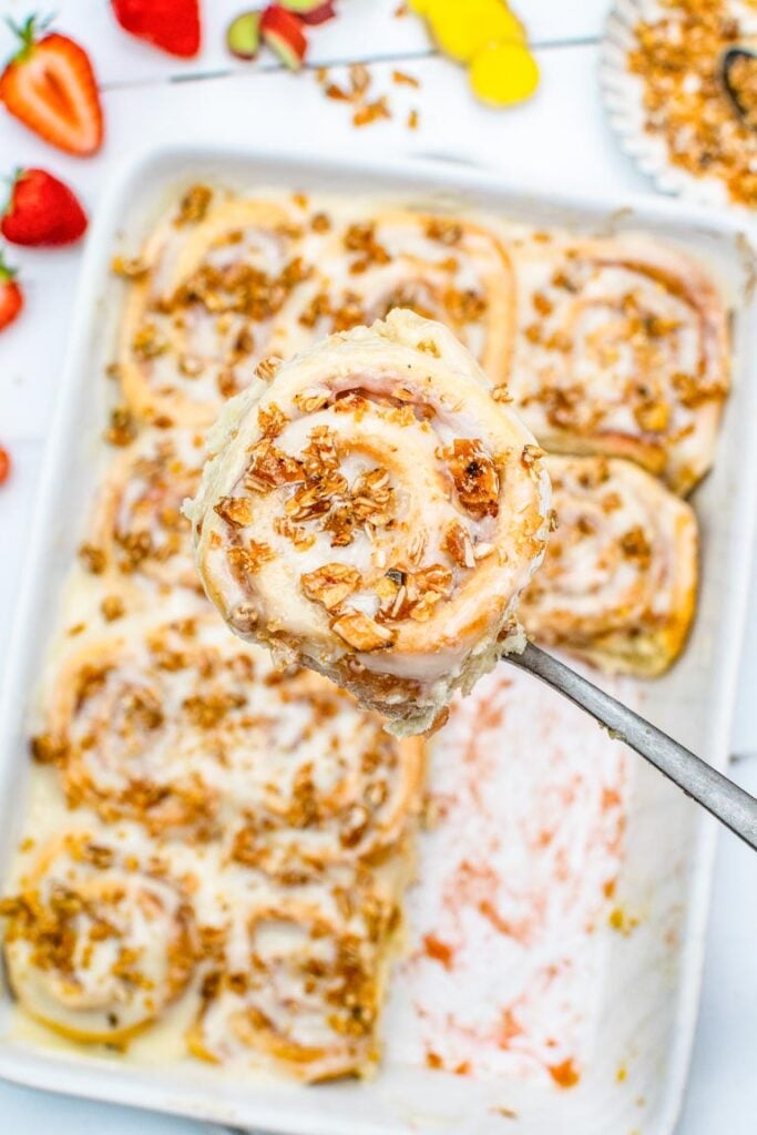 A glazed sweet roll with a cream cheese and almond praline topping being lifted from a baking tray