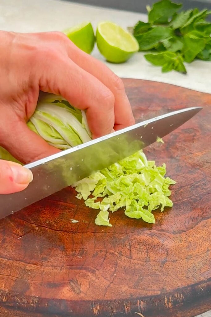 Shredding Chinese leaf cabbage into thin strips on a wooden cutting board