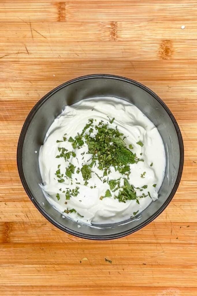 Thick white yogurt in a black bowl topped with chopped fresh mint leaves