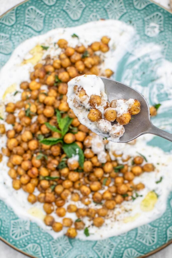 Roasted chickpeas on a bed of creamy white sauce with a spoonful being lifted
