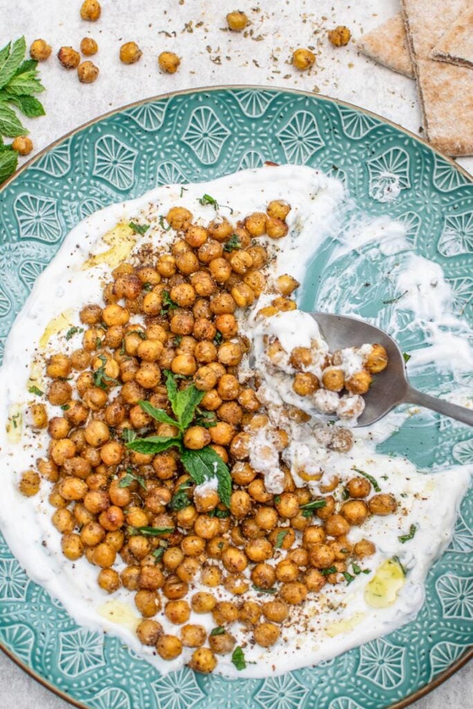 Roasted spiced chickpeas on a bed of creamy yogurt sauce with fresh mint and a spoon taking a scoop