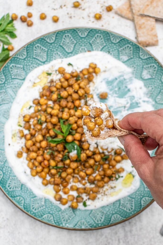 Roasted chickpeas on a bed of creamy sauce, with a hand dipping a piece of pita bread into the dish