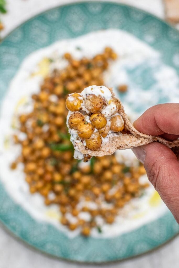 Pita bread topped with roasted chickpeas and creamy white sauce held over a plate