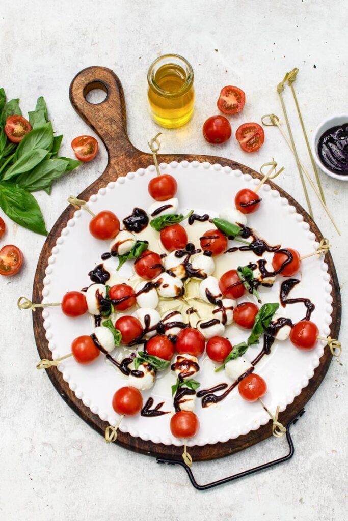 Caprese skewers with cherry tomatoes, mozzarella, and basil drizzled with balsamic glaze on a white plate