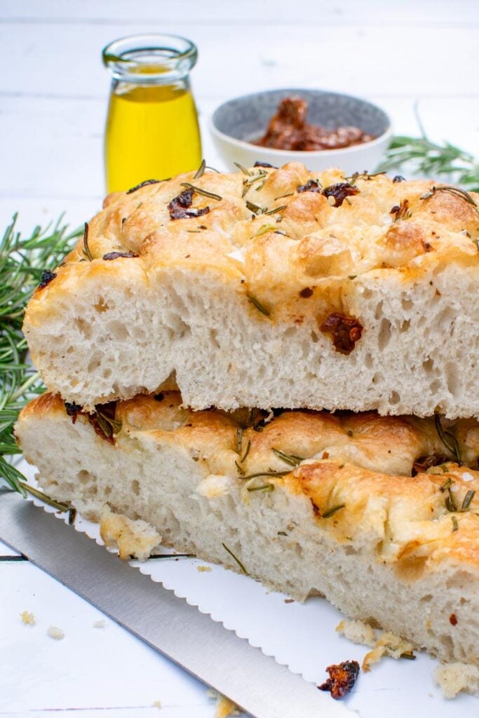 Two thick slices of rosemary and sun-dried tomato focaccia bread showing an airy, porous crumb
