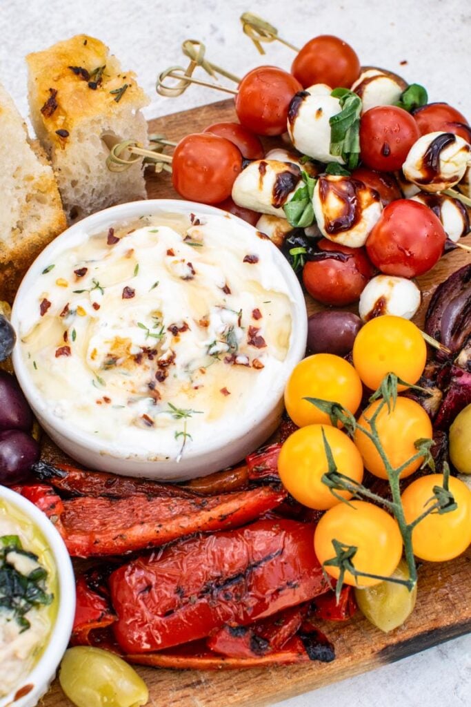 Antipasti board with Caprese skewers, whipped cheese dip, roasted red peppers, yellow tomatoes, and focaccia