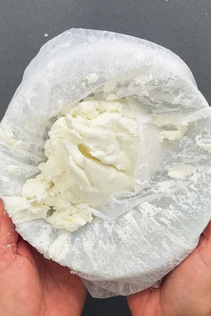 Thick strained labneh cheese held in a cheesecloth, showing the creamy texture after draining