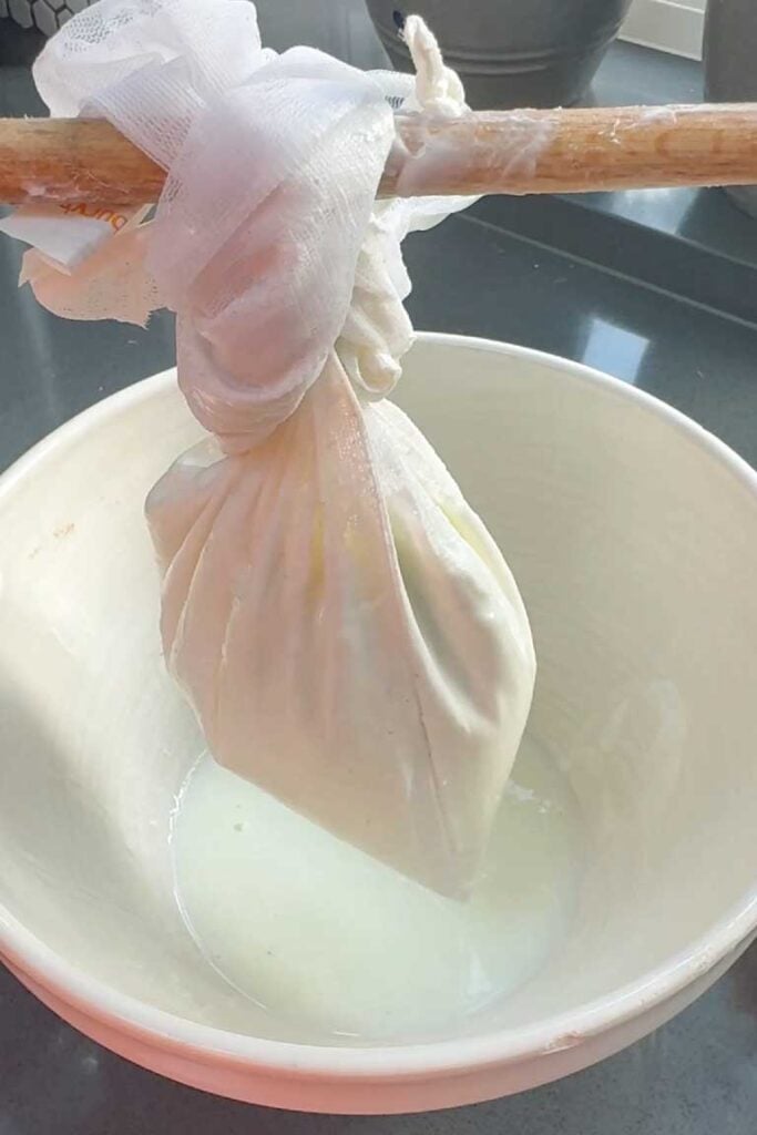 Yoghurt being strained through a cheesecloth over a white bowl to make labneh