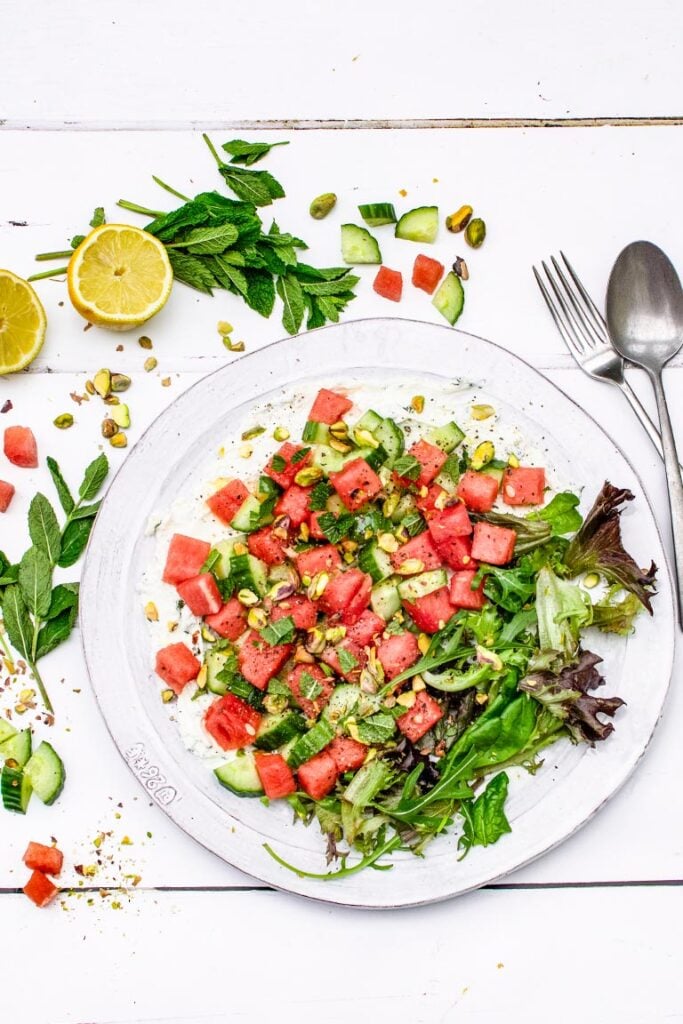 Assembled watermelon cucumber salad on a white plate with mint and lemon, overhead flat lay