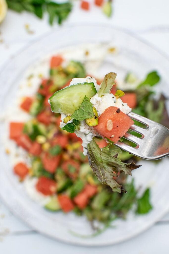 Close-up of a fork holding a bite of watermelon cucumber salad with labneh and pistachios