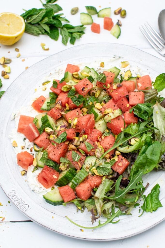 Close-up overhead view of watermelon and cucumber salad with labneh, pistachios and fresh herbs