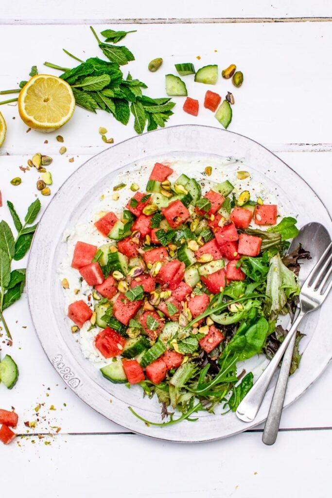 Watermelon cucumber salad with minty labneh, pistachios and fresh mint on a white plate, overhead view