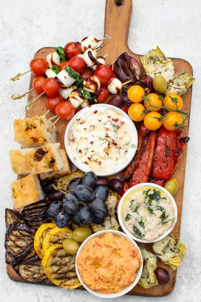 Overhead shot of an antipasto platter with grilled vegetables, dips, olives and focaccia