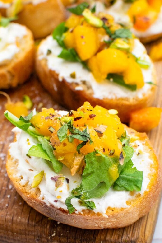 Close-up of peach bruschetta topped with rocket, diced peach and crushed pistachios