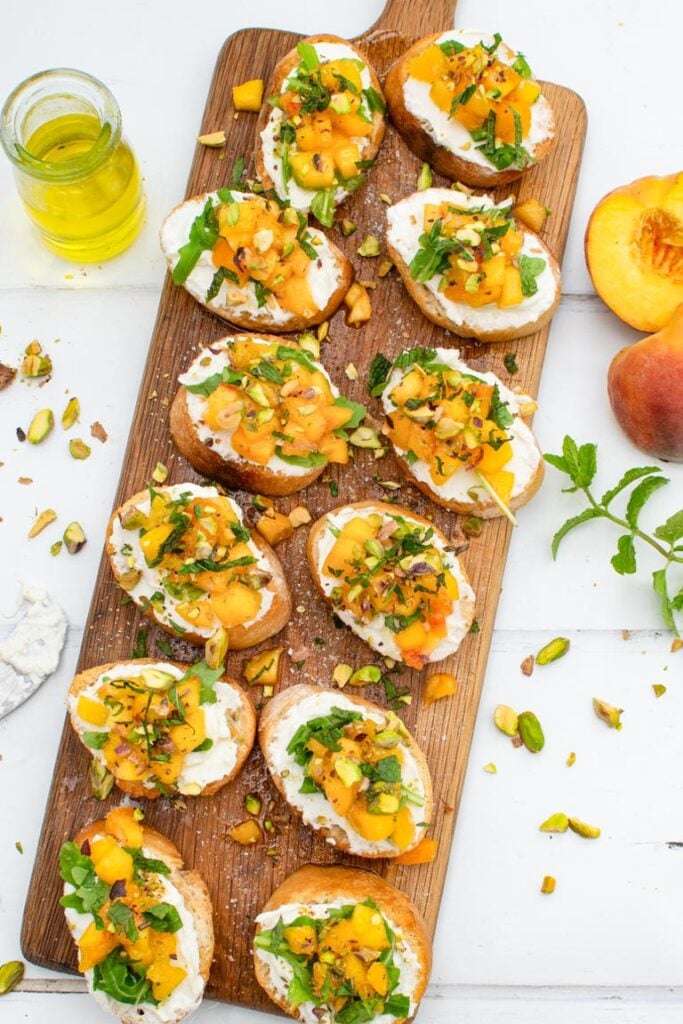 Peach bruschetta with whipped ricotta, pistachios and mint on a serving board