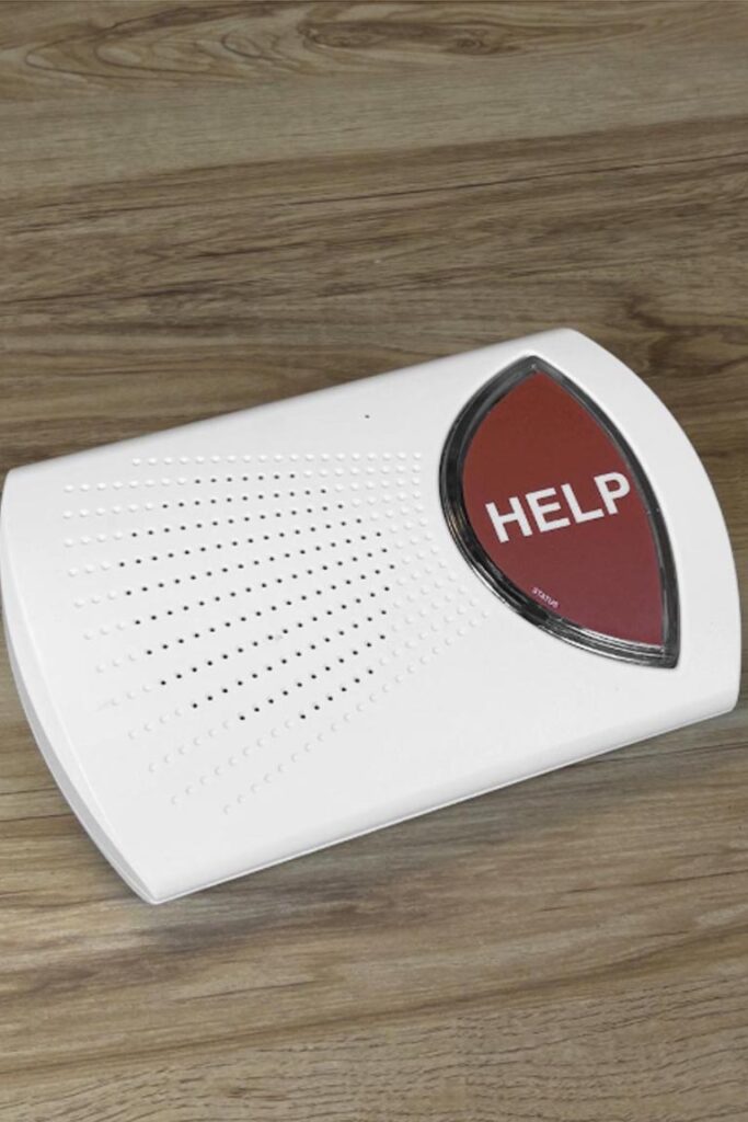 White home medical alert base unit with a red HELP button on a wooden surface