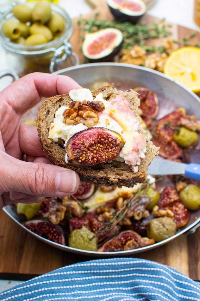 hand holding bread with roasted figs and feta