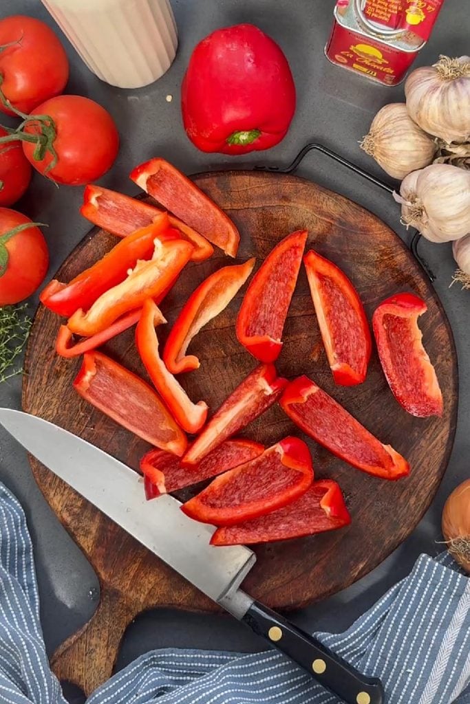 red pepper cut in eighths and deseeded on wooden chopping board with knife