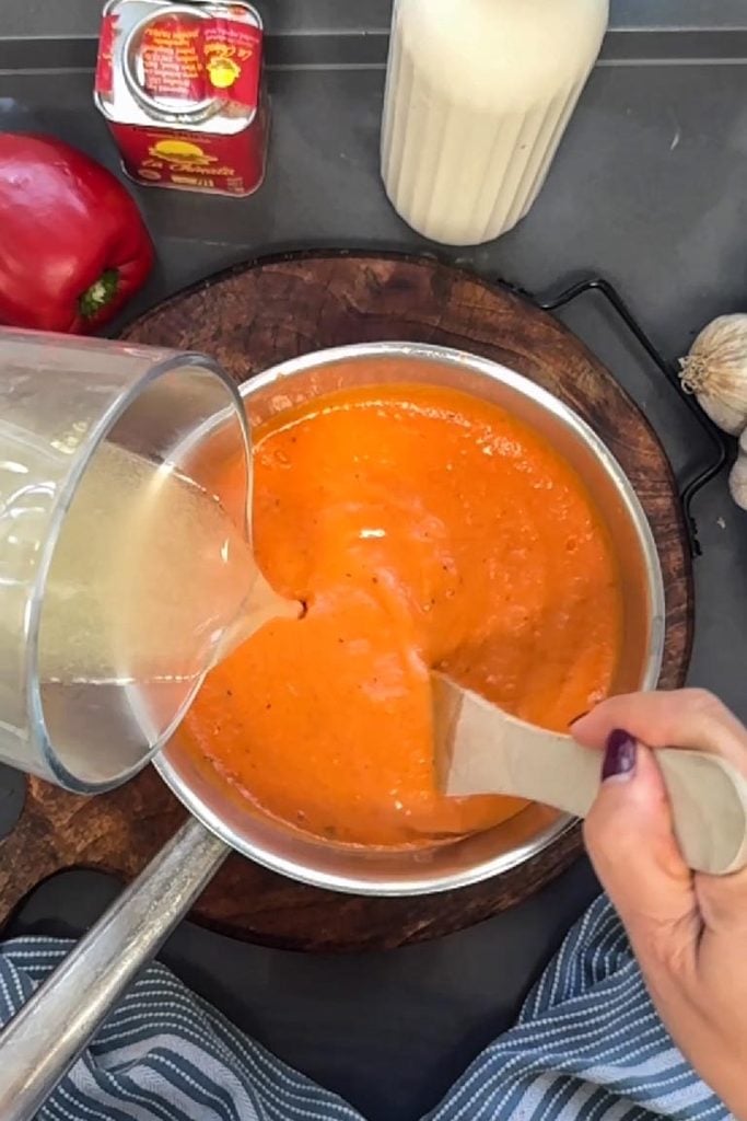 adding vegetable stock to roasted red pepper and tomato soup