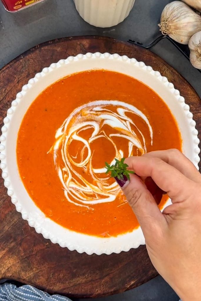 garnishing roasted red pepper and tomato soup with cream and thyme