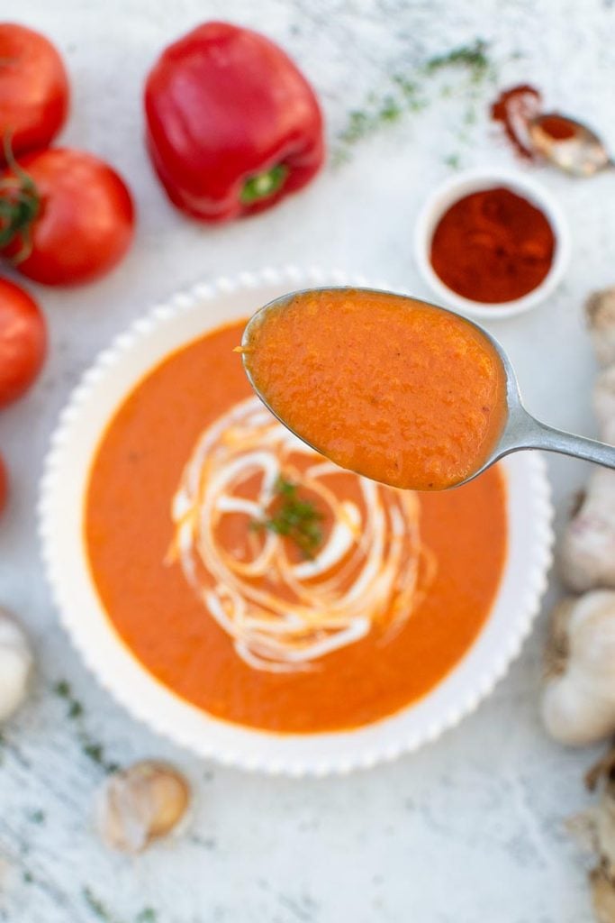 close up of roasted red pepper and tomato soup on spoon with dairy-free cream and thyme