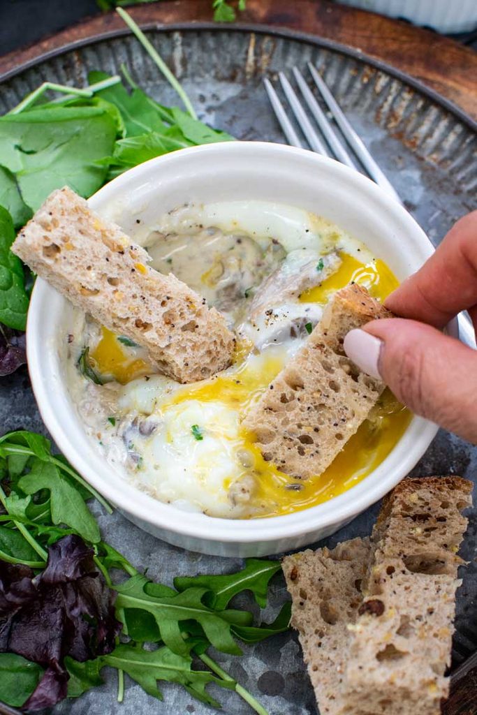 Bread soldier dipped into the runny yolk of a baked egg with creamy mushrooms