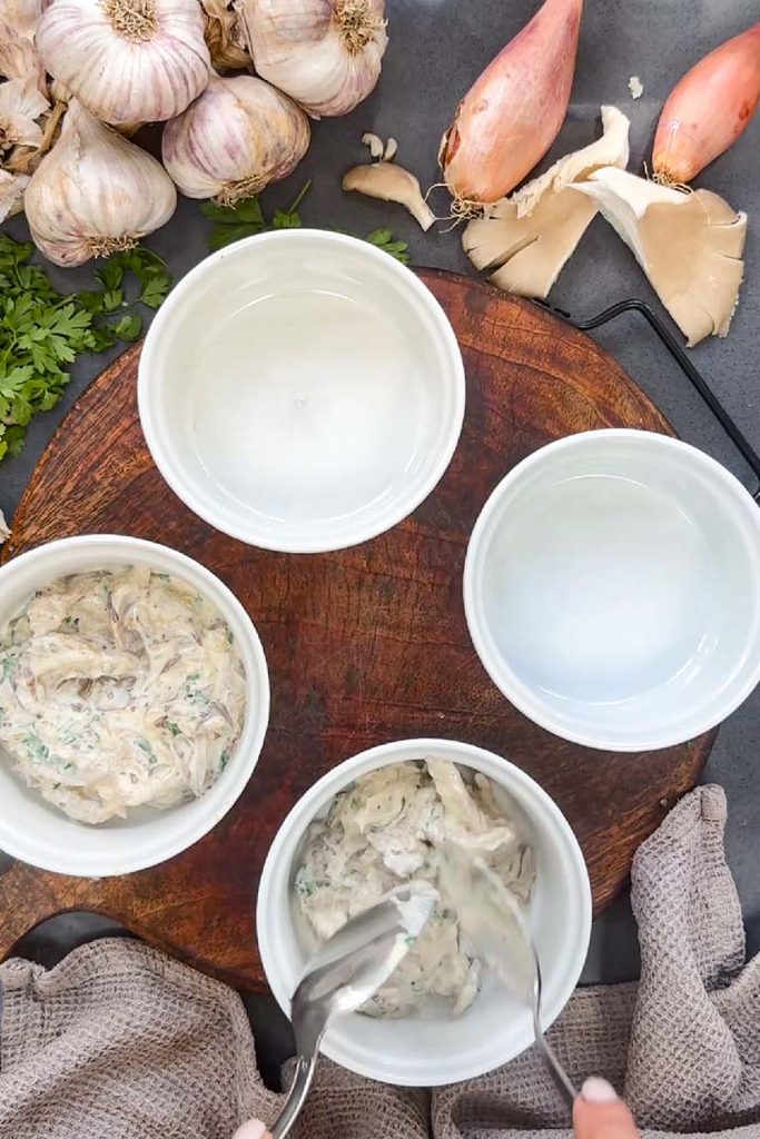 Creamy mushroom, mustard and parsley mixture being spooned into four white ramekins