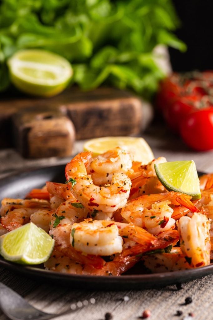 Grilled garlic and herb prawns with lime wedges on a dark plate, part of a sustainable flexitarian diet