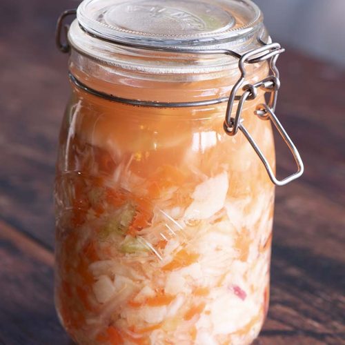 A glass jar of homemade fermented vegetables with shredded cabbage, carrot, apple and ginger