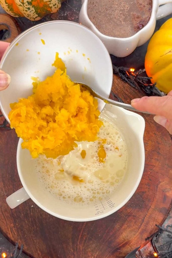 Pumpkin purée being whisked into plant-based milk, oil and vanilla extract in a jug