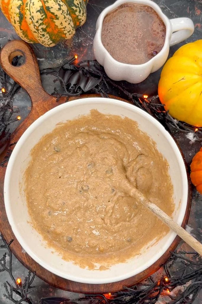 Thick pumpkin pancake batter with chocolate chips stirred together in a white mixing bowl