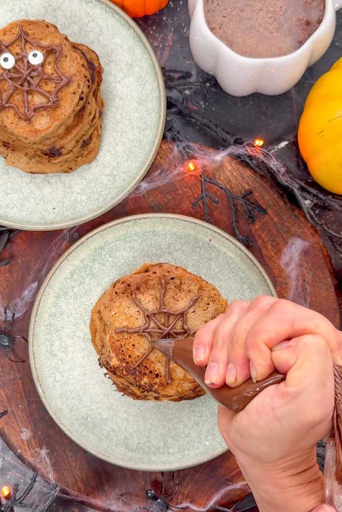 Piping chocolate across the lines on a pancake stack to form a spider web pattern