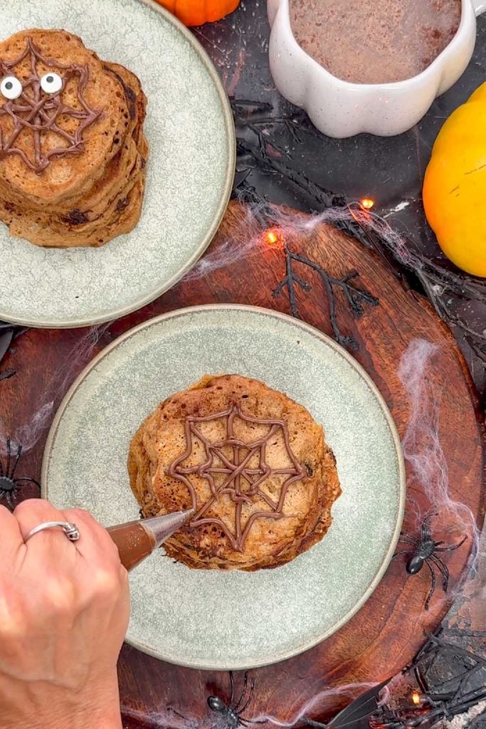 Finishing the chocolate spider web design on top of a stack of pumpkin pancakes