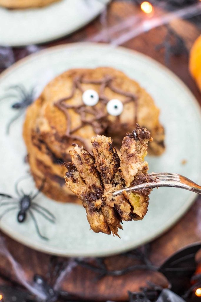 Fork lifting a fluffy bite from a stack of vegan pumpkin Halloween pancakes decorated with a chocolate spider web and edible eyes