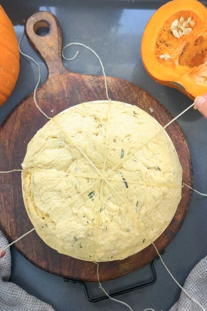 Pumpkin bread dough tied with four lengths of kitchen twine crossing in the centre like wheel spokes to create the pumpkin shape