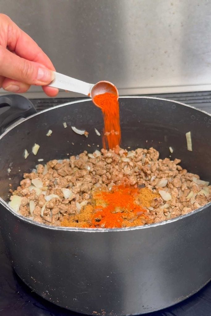 Spices being added to browned Quorn mince and onion in a large stockpot for taco soup