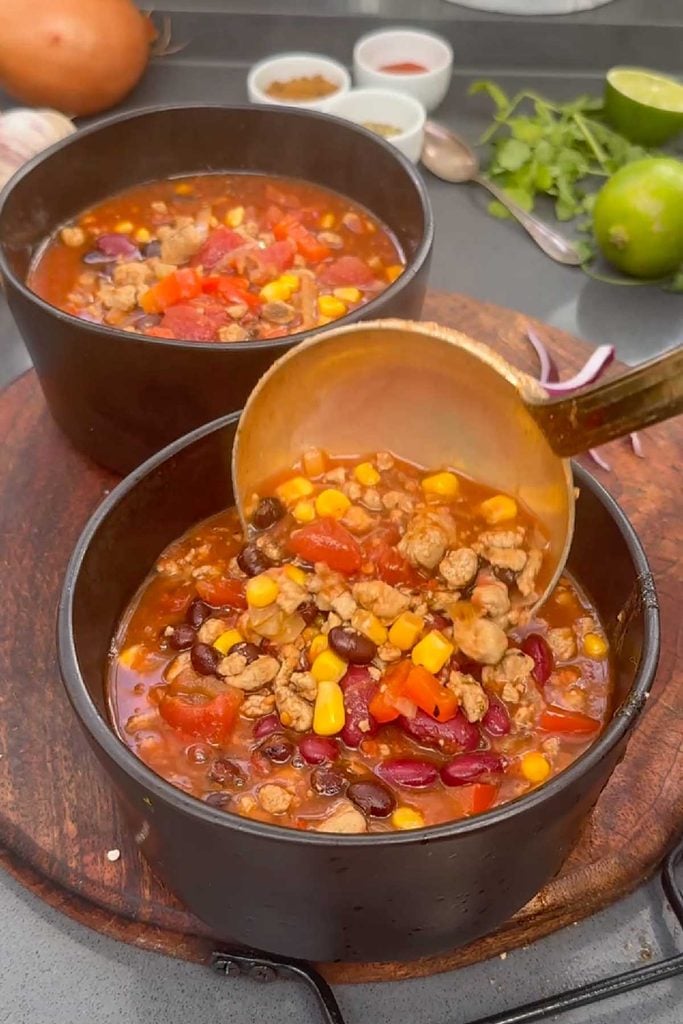 Ladling vegetarian taco soup with black beans, kidney beans and sweetcorn into a bowl