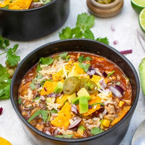Two bowls of vegetarian taco soup topped with tortilla chips, avocado, red onion, grated cheese, coriander and jalapeños
