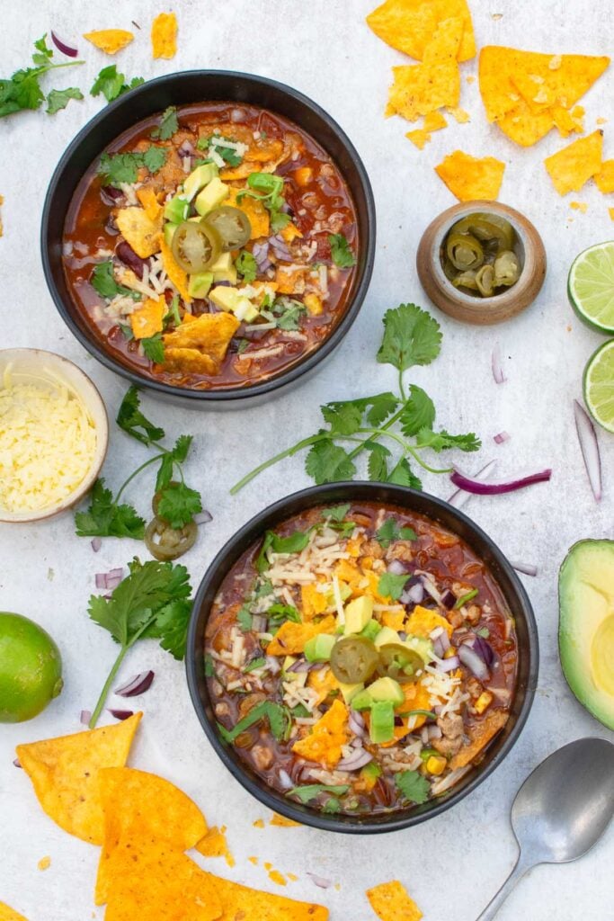 Overhead view of two bowls of taco soup with tortilla chips, limes and a pot of sliced jalapeños